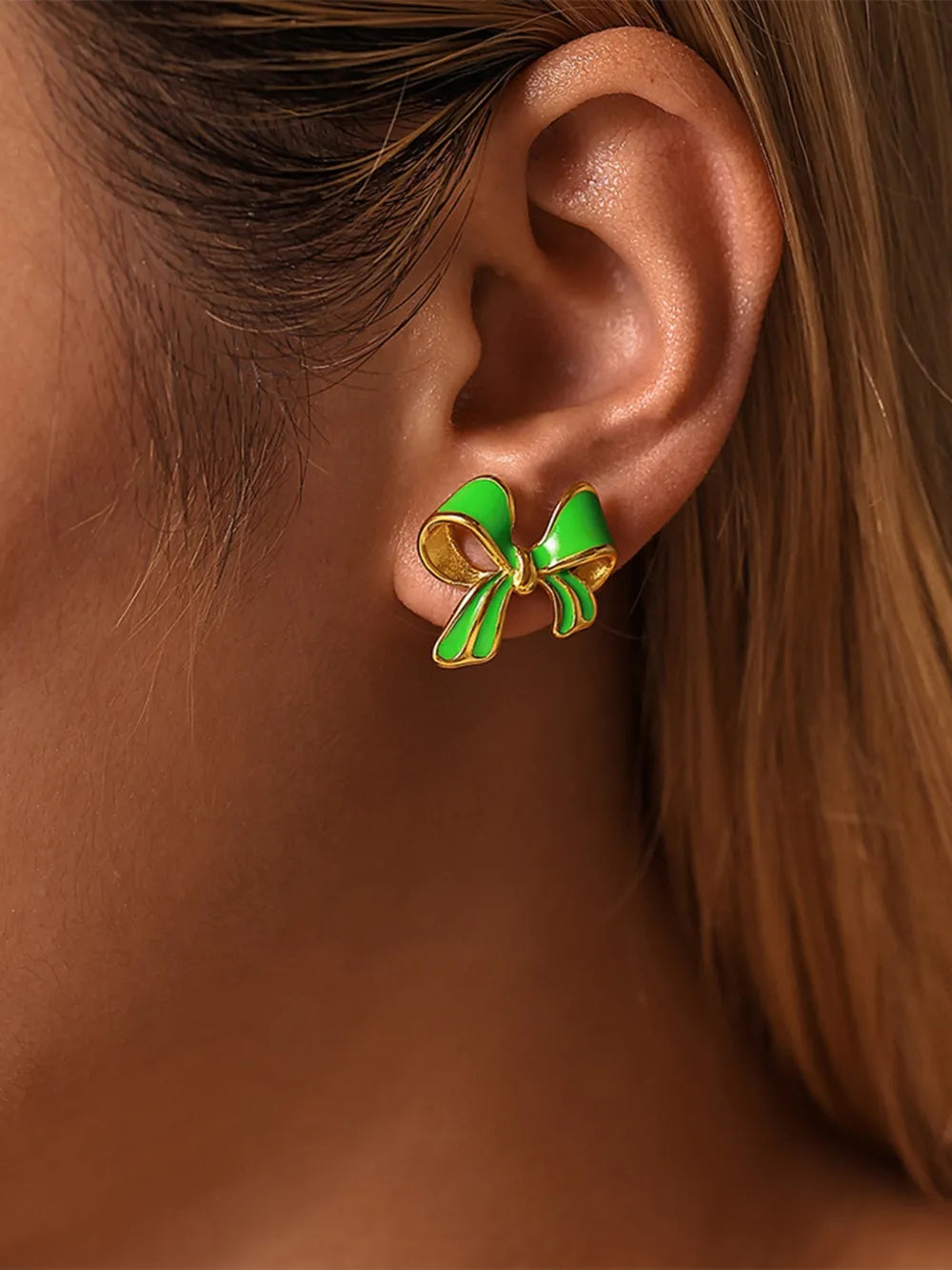 Close-up of a green and gold 18K gold-plated bow stud earring worn on the ear, elegant and stylish accessory.