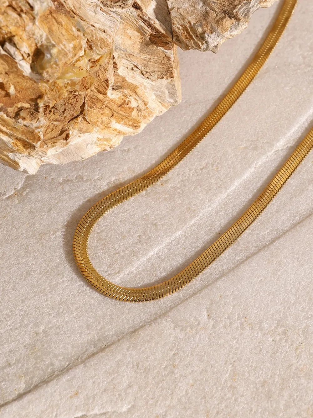 Close-up of a gold-plated chain from the three-layered cross necklace resting on a textured stone surface.