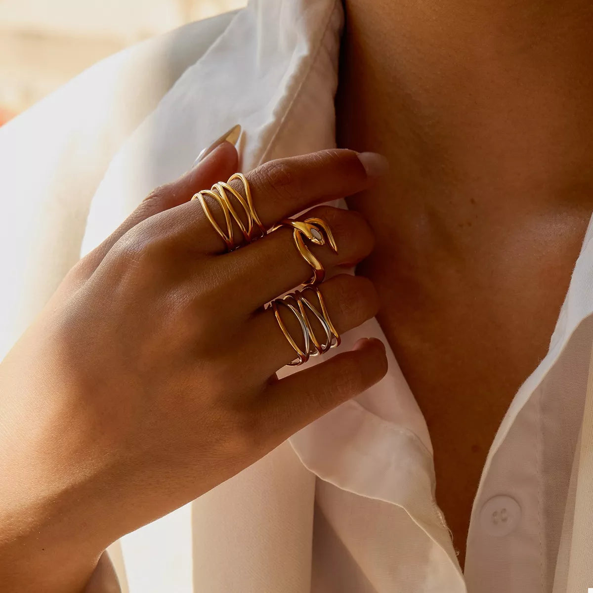 Close-up of a hand wearing an adjustable two-tone open ring made of 18K gold-plated stainless steel on a white shirt background