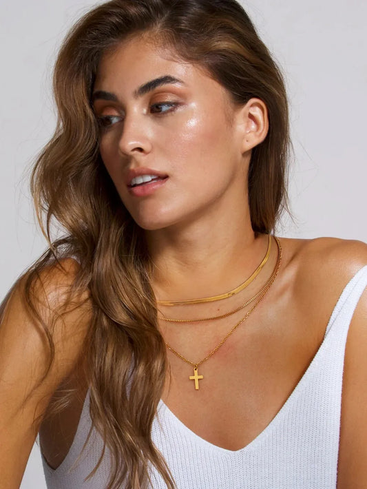 Model wearing an 18K gold-plated three-layered cross necklace with varying chain styles and lengths.