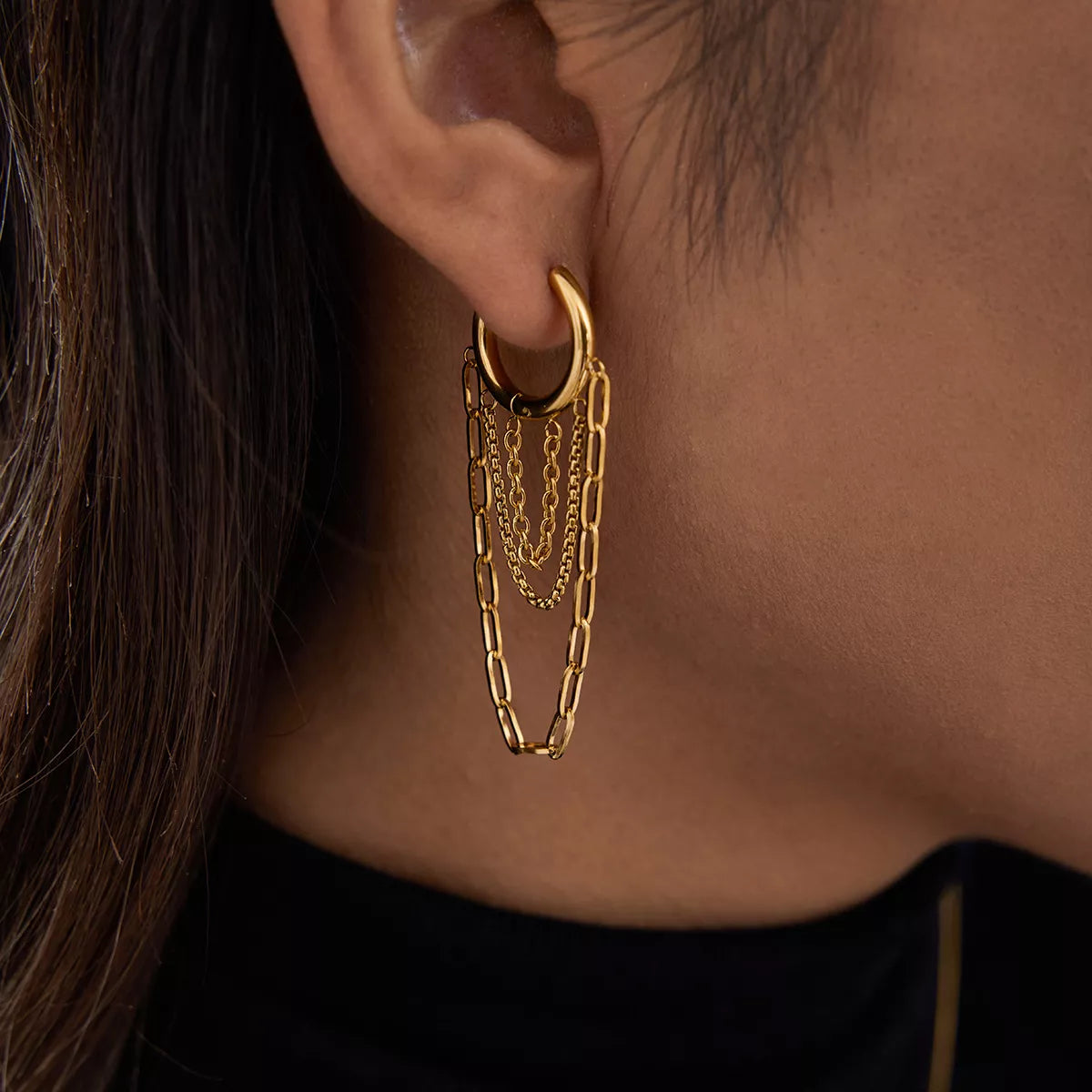 Close-up of a gold-plated chain hoop earring on a person’s ear showcasing layered chain design