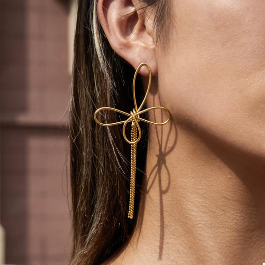 Close-up of a woman's ear wearing an 18K gold plated stainless steel tassel bow drop earring in natural light