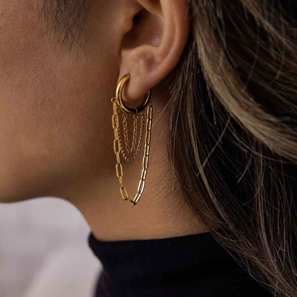 Close-up of an ear wearing 18K gold-plated chain hoop earrings with layered delicate chains on a stainless steel hoop